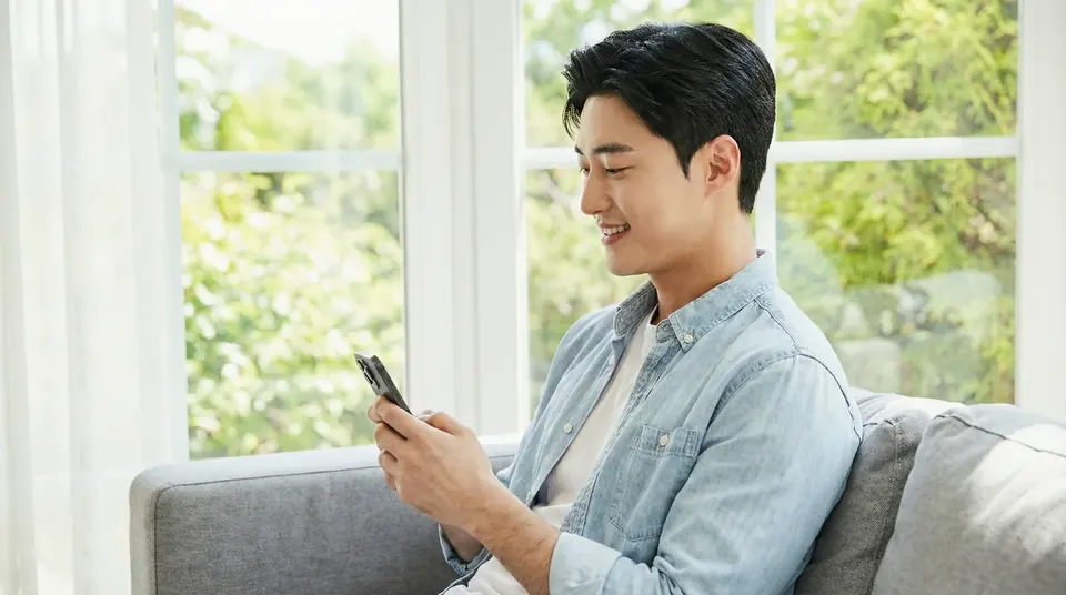 소파에 앉아 휴대전화로 안내 문자를 읽는 남성